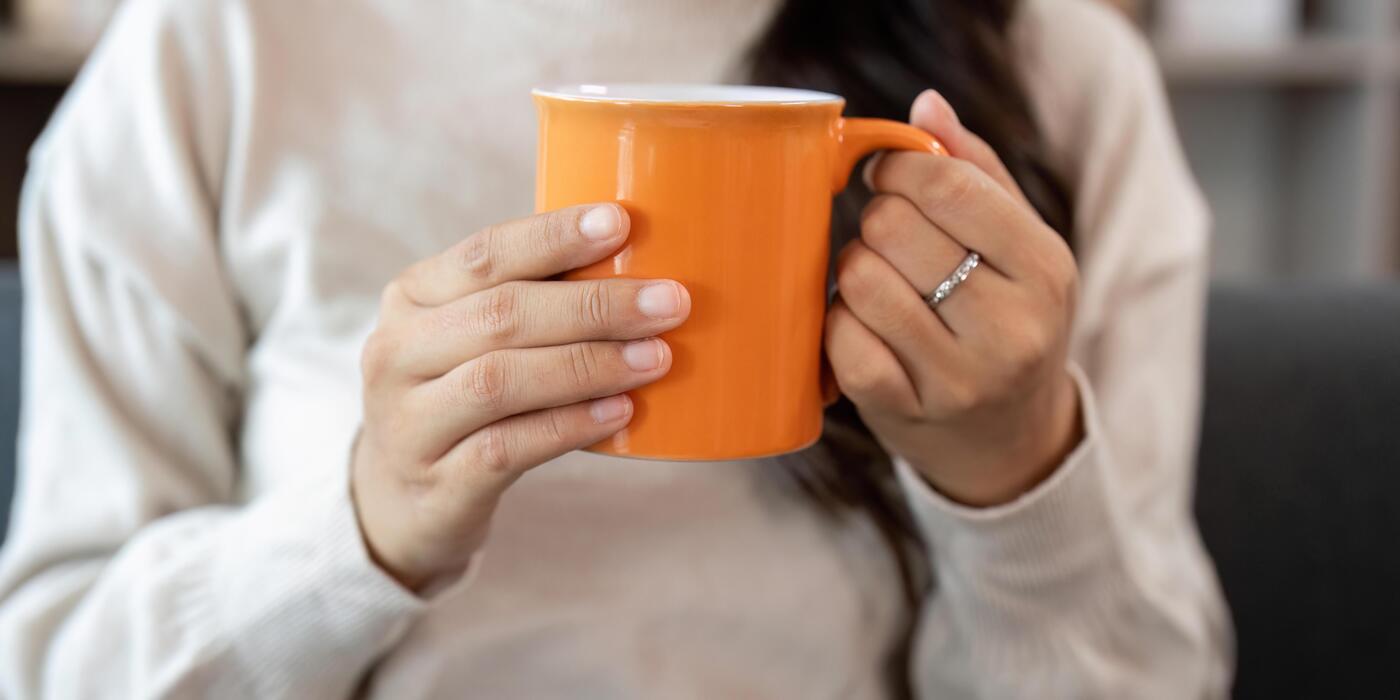 Hands holding a warm ceramic mug near a sunlit window